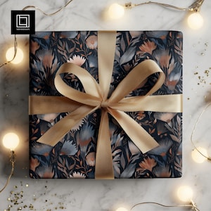 May include: A wrapped gift with a dark blue floral pattern, tied with a gold ribbon. The gift is surrounded by string lights and gold confetti on a marble surface. The floral design includes blue, peach, and white flowers and leaves.