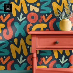 May include: A coral-colored nightstand with a drawer and a dark knob stands against a wall covered in a colorful, abstract pattern. A yellow vase with greenery sits on the nightstand. The wall pattern features shapes in yellow, teal, orange, and red.