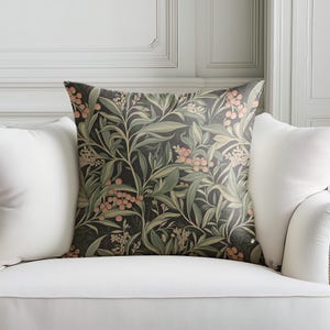 Könnte beinhalten: Ein dekoratives Kissen mit einem dunkelgrünen und rosafarbenen Blumenmuster. Das Kissen zeigt ein sich wiederholendes Muster aus Blättern und Beeren.