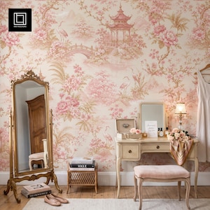 May include: A room interior featuring a tall gold-framed floor mirror, a light-coloured wooden vanity table with a mirror, a matching upholstered stool, and a small wicker side table. The walls are covered in wallpaper with a pink floral pattern.