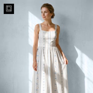 Könnte beinhalten: Ein ärmelloses, bodenlanges Kleid mit quadratischem Ausschnitt und figurbetontem Oberteil. Der weiße Stoff ist mit vertikalen Streifen aus sich wiederholenden blauen Blumenmustern und kleinen Schleifenmotiven versehen, was eine strukturierte Silhouette ergibt.