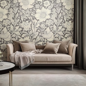 Puede incluir: Un sofá beige claro con un papel tapiz con estampado floral detrás. El sofá tiene una manta y tres almohadas. Las almohadas son de color marrón claro.