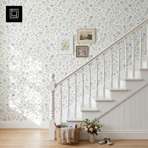 Peut inclure: Papier peint avec un motif répétitif de petites fleurs sauvages bleues et jaunes sur fond blanc. Un escalier en bois blanc avec une rampe est placé devant le mur. Deux cadres sont accrochés au mur au-dessus de l'escalier.