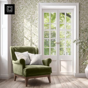 Könnte beinhalten: Ein grüner Samtsessel mit zwei gestreiften Kissen steht vor einer weißen Doppeltür. Der Raum hat einen hellen Holzboden und Tapeten mit einem grünen Blättermuster. Die Tür öffnet sich zu einer Aussicht auf grüne Bäume.