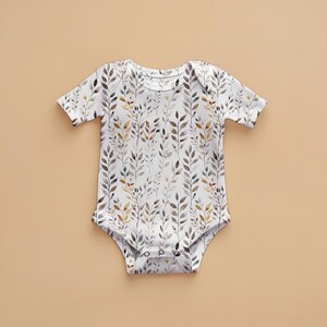 May include: A white baby onesie with a watercolor pattern of brown, gray, and yellow leaves.