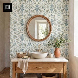 Peut inclure: Intérieur de salle de bain avec un meuble-lavabo en bois, un plan de travail en marbre et un miroir rond en bois. Le papier peint présente un motif floral bleu et vert. Un lavabo blanc, un vase en terre cuite avec de la verdure et un panier en osier sont également visibles.