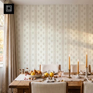 May include: A dining room scene featuring a wooden table with a white runner, a bowl of pears and walnuts, two yellow quince, a glass, and three tall yellow taper candles in metal holders against a wall with cream and beige floral striped wallpaper.