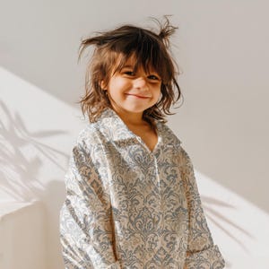 May include: A young person wearing a light blue and cream patterned shirt with a V-neck collar. The shirt has a damask pattern.