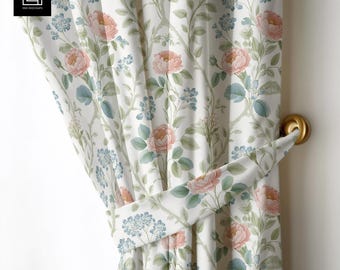 Puede incluir: Cortina con estampado floral y recogedor. La cortina blanca presenta un patrón repetido de rosas rosas, flores azules y hojas verdes. Se ve un recogedor de cortina dorado.