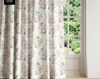 Puede incluir: Cortinas florales color crema con un patrón repetido de rosas rosas, detalles azules y follaje amarillo. Las cortinas cuelgan frente a una ventana con vistas a un jardín.