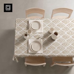 Puede incluir: Vista aérea de una mesa de comedor para dos. La mesa está cubierta con un mantel con estampado beige y blanco. Dos cubiertos incluyen platos, servilletas y pequeñas tazas de cerámica. Se ven dos sillas de madera.