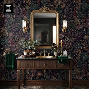 Può includere: Un bagno con carta da parati floreale scura, uno specchio con cornice dorata e un mobiletto in legno. Il mobile ha un piano nero, un lavandino dorato e bottiglie. Asciugamani verdi sono appesi a un portasciugamani dorato. Due applique affiancano lo specchio.