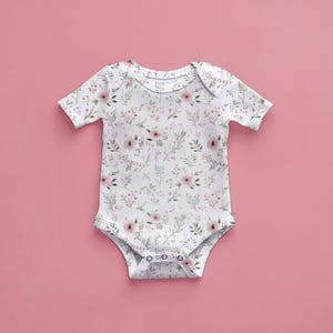 May include: A white baby onesie with a pink floral pattern. The onesie has short sleeves and a snap closure at the bottom.
