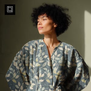 May include: A long-sleeved robe featuring a dark blue-gray base color with a repeating pattern of light green and cream-colored leaves. The garment has a V-neckline, a wrap-style front closure with a tie waist, and voluminous sleeves.