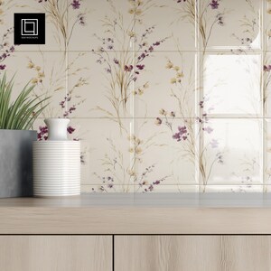 May include: Cream-coloured floral tile backsplash featuring a repeating pattern of purple and yellow wildflowers. A white vase and a potted plant sit on a light wood surface in front of the tiles. The logo "1001 Mockups" is in the top left corner.