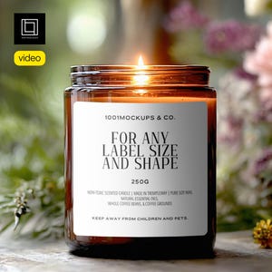 Op de afbeelding: Een brandende, amberkleurige glazen potkaars met een wit etiket. Het etiket luidt "FOR ANY LABEL SIZE AND SHAPE" en "250G". De kaars is omgeven door groen en bloemen. De tekst "1001 MOCKUPS & CO." is ook zichtbaar.