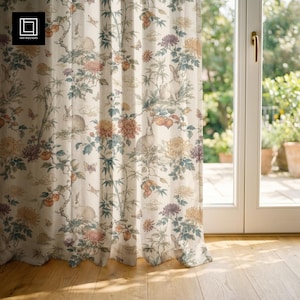 May include: Cream-colored curtain with a botanical print featuring rabbits, flowers, and fruit. The design includes peach, yellow, and purple floral elements, along with green foliage and butterflies. The curtain hangs in front of a window with a view of a garden.