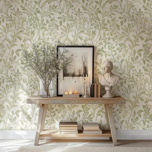 May include: A wooden console table with a white background featuring a green floral wallpaper pattern. The table has two shelves and is decorated with a framed black and white photograph, a bust of a woman, candles, and books.
