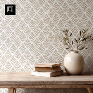 Puede incluir: Una composición de naturaleza muerta con una mesa de madera, libros y un jarrón de cerámica beige con ramas de olivo. El fondo es un papel pintado con un patrón de hojas repetido en beige y blanco. El logo "1001 Mockups" está en la esquina superior izquierda.