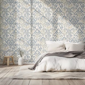 May include: A white bed with a gray throw blanket and white pillows sits in front of a wall with a blue and beige damask pattern wallpaper.