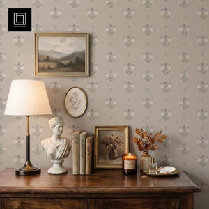 May include: A table lamp with a beige shade, a white bust sculpture, three books, a framed landscape painting, a framed botanical sketch, a candle in a glass jar, a small vase with dried branches, and a glass bottle on a wooden surface.