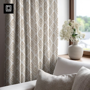 Puede incluir: Cortina estampada en beige y blanco con un diseño de hojas. La cortina está colgada frente a una ventana. Un jarrón blanco con flores blancas está en el alféizar. Un sofá blanco con cojines está en primer plano.