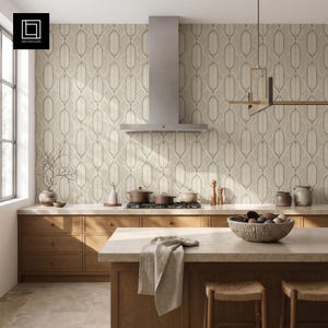 Può includere: Una cucina con mobili in legno chiaro, una cappa in acciaio inossidabile e carta da parati beige con motivo geometrico. Un'isola cucina con piano in pietra, un panno in lino e una ciotola con sfere decorative.