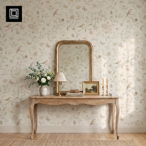 May include: A light wood console table with curved legs, topped with a tall arched mirror, a small lamp with a pleated shade, a framed landscape painting, and a ceramic vase filled with white flowers against floral wallpaper.