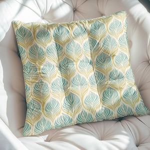 Puede incluir: Una almohada decorativa con un patrón de hojas verde azulado y dorado. La almohada está hecha de una tela suave y texturizada con un brillo sutil.