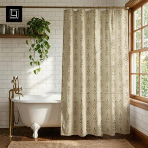 May include: A beige shower curtain with a repeating pattern of stylized brown leaves. The curtain hangs in front of a white bathtub with brass fixtures. A wooden shelf holds plants and metal buckets.