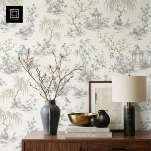 May include: A room interior with a dark wooden cabinet, a gray vase with branches, a gold bowl, and a black sculpture. A lamp with a marble base sits on the cabinet. The wallpaper features a blue and white Asian landscape.