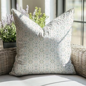 Puede incluir: Una almohada blanca con un patrón floral de color azul claro y rosa. La almohada está sentada en una silla de mimbre.
