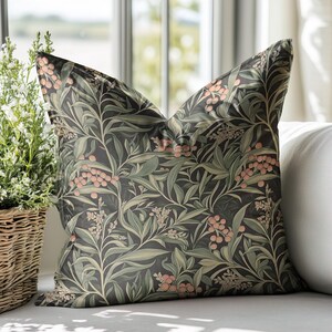 May include: A decorative throw pillow with a dark green background and a floral pattern featuring pink berries and green leaves.