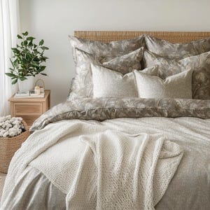 Peut inclure: Une couverture en tricot blanc drapé sur un lit avec une housse de couette à motifs et plusieurs oreillers à motifs. Le lit a une tête de lit en bois.