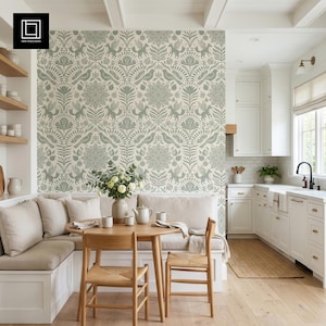 Peut inclure: Une cuisine avec un sol en bois clair, des armoires blanches et une table ronde en bois avec deux chaises en osier. Le mur est orné d'un papier peint à motifs verts et blancs. Un banc intégré avec des coussins beiges est également présent.