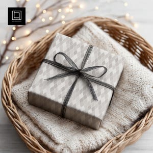 May include: A wrapped gift box with a gray diamond pattern and a black ribbon bow sits in a woven basket atop a white knitted blanket. The basket is brown and the background has soft, blurred lights.