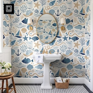 May include: A bathroom features wallpaper with a nautical pattern of blue and tan fish, sailboats, anchors, seashells, and starfish. A white pedestal sink with a monogrammed towel sits below an oval mirror. A wooden stool and basket are present.