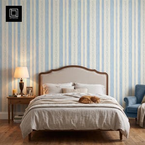 May include: Wallpaper featuring vertical stripes in alternating shades of light blue and cream, accented by a delicate leaf vine pattern. The design is displayed in a bedroom setting with a bed, a wooden nightstand, a lamp, and a blue armchair.