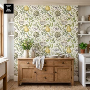 May include: A wooden sideboard with drawers and doors is in a kitchen setting. The wallpaper features a repeating pattern of pears, artichokes, birds, and other botanical elements. A vase of flowers and a stack of plates are on the sideboard.