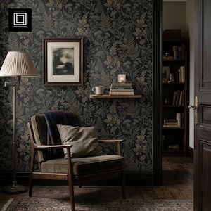 May include: A cozy living room scene featuring a dark floral wallpaper with fern and thistle patterns. An olive green armchair with a throw and pillow sits near a floor lamp. A framed picture and a shelf with books and a candle add to the room's ambiance.