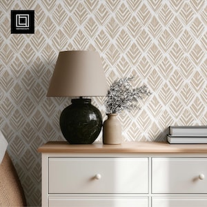 May include: A beige lampshade sits atop a dark green lamp base on a wooden surface. A small vase with greenery and a stack of books are also on the surface. The background features a patterned wallpaper in beige and white.