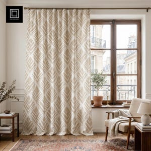Può includere: Tenda beige e bianca a motivi di foglie davanti a una finestra. La tenda presenta un motivo a foglie ripetuto. La finestra si affaccia su una città europea. Un tavolino, una sedia e un tappeto sono davanti alla finestra.