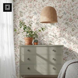 May include: A light green dresser with three drawers, topped with potted plants, sits in front of floral wallpaper. A woven pendant light hangs above. The wallpaper features pink flowers, birds, and cranes.