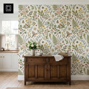 May include: A kitchen scene featuring floral wallpaper with birds, butterflies, and flowers. A dark wooden cabinet with a vase of white flowers and a bowl sits below the wallpaper. The room has a window and wooden flooring.