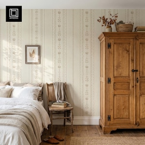 May include: A bedroom scene featuring a tall wooden wardrobe, a bed with white bedding and a beige throw blanket, and a wooden chair with a draped cloth. The wall is covered in wallpaper with vertical stripes of floral and dotted patterns.