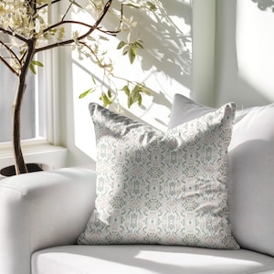 May include: A white sofa with a decorative cushion featuring a light blue and beige patterned design. The cushion is sitting on the sofa against a white background.