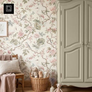 Può includere: Un armadio in legno color verde salvia chiaro si trova accanto a un cesto di vimini contenente un coniglio di peluche e blocchi di legno. La parete presenta una carta da parati con fiori rosa, foglie verdi e gru bianche su fondo crema.