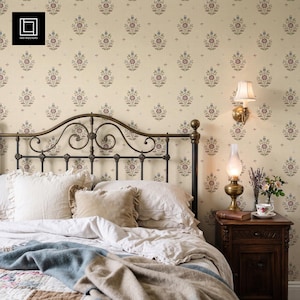May include: A bedroom scene featuring a dark metal headboard with scrollwork, cream-colored bedding, and a blue-toned throw blanket. The wall is covered in cream wallpaper with a repeating floral pattern in muted red, blue, and green tones.