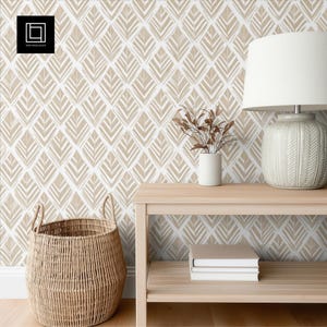 Puede incluir: Una escena interior de tonos neutros con una cesta tejida, una mesa auxiliar de madera y papel pintado estampado. El papel pintado tiene un diseño geométrico repetitivo en beige y blanco. Una lámpara blanca y un pequeño jarrón con tallos secos están sobre la mesa.