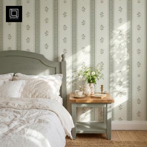 Può includere: Una camera da letto con testiera in legno verde salvia, biancheria da letto bianca e un comodino coordinato. La parete è rivestita con carta da parati color crema a strisce verticali con motivi floreali verdi e sottili linee decorative.